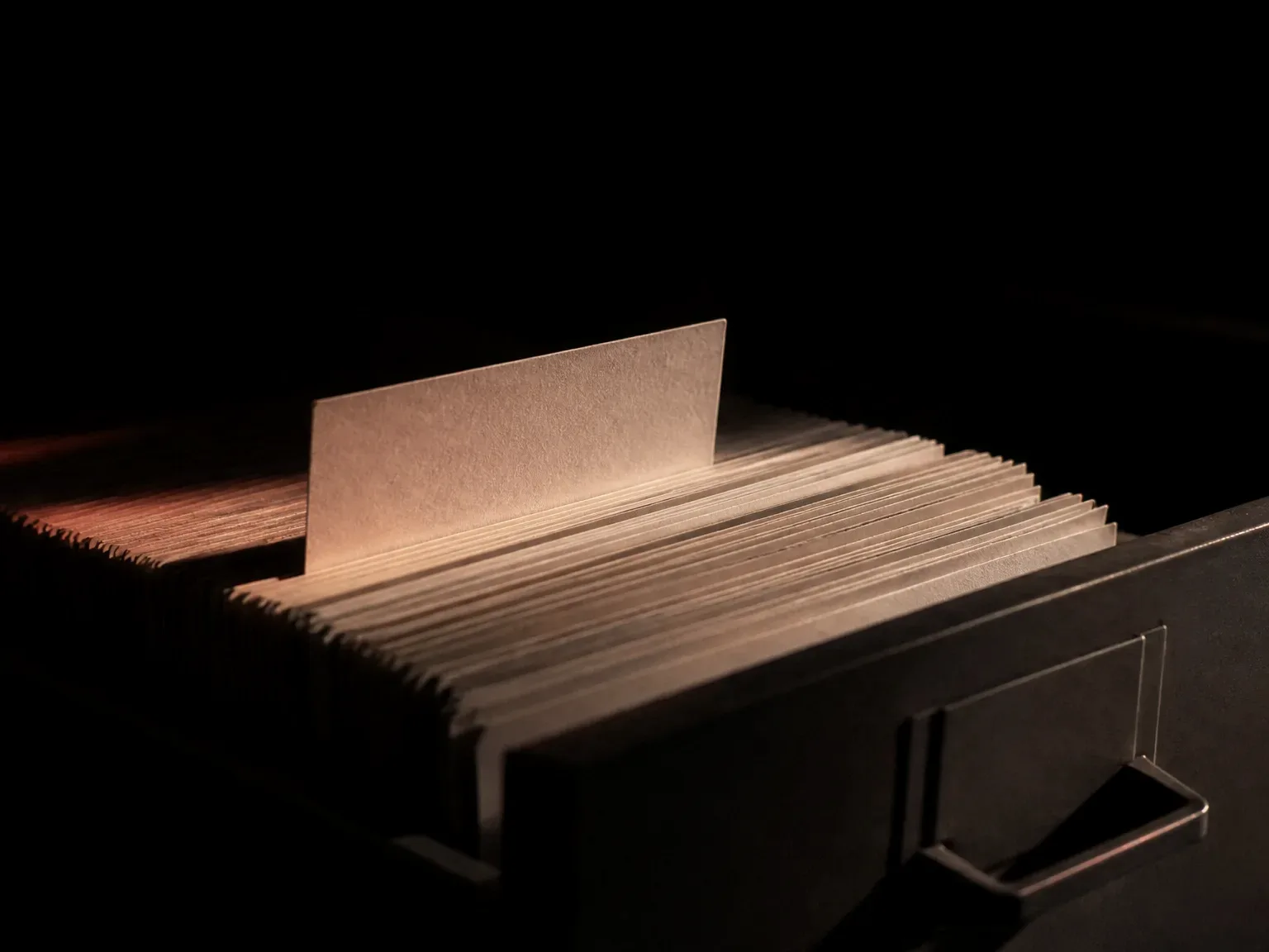 Cajón de archivo entreabierto con fichas alineadas y una elevada bajo la luz